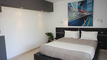 A modern bedroom with a large bed, a cityscape painting, and a small plant.