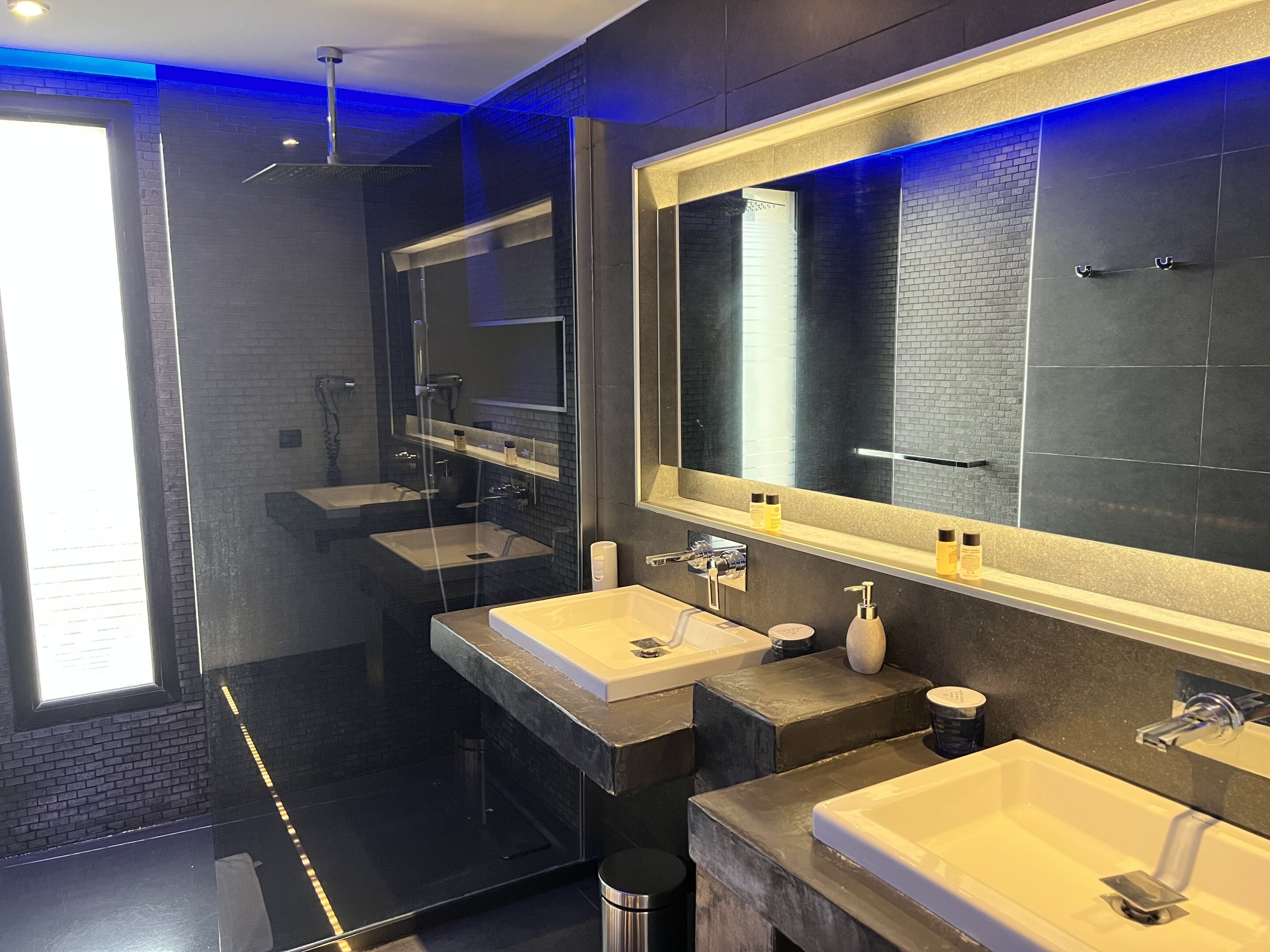 Ein modernes Badezimmer mit zwei Waschbecken, einem großen Spiegel und einer Duschkabine.