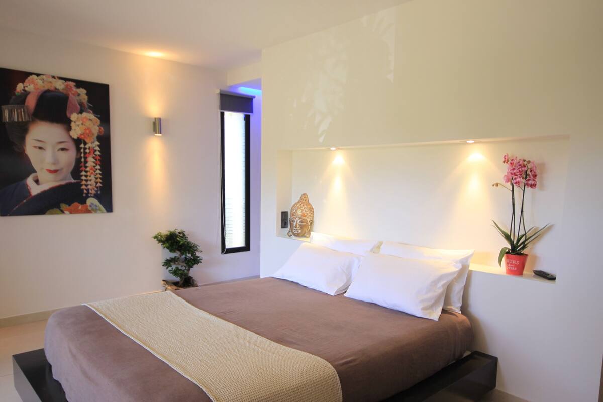 A modern bedroom with a large bed, a wall-mounted TV, a small potted plant, and a decorative item on the wall.