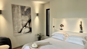 A modern bedroom with a large bed, a wall-mounted shelf with decorative items, and a framed artwork above the bed. - Nature ET Design (Bonifacio)