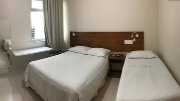 Une chambre d’hôtel avec deux lits simples, une tête de lit en bois, une table de chevet avec une lampe et une fenêtre avec des rideaux.