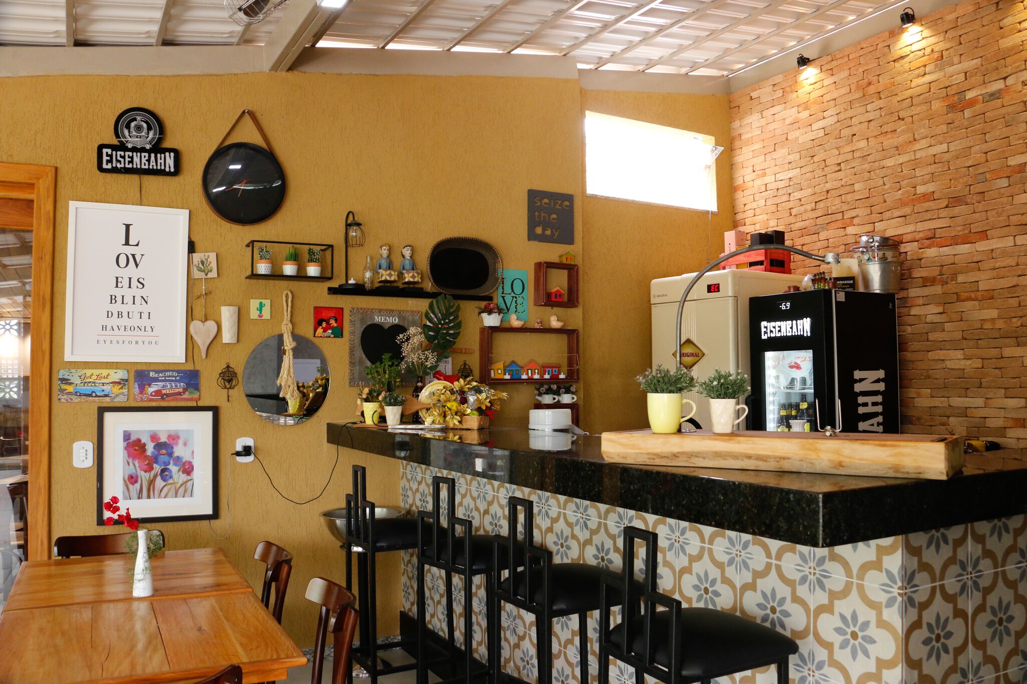 Zona de bar acollidora amb un taulell de fusta, tamborets negres i una paret de maó.
