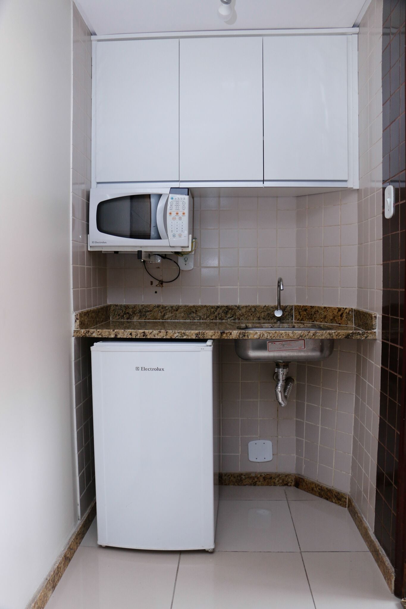 Cocina compacta con microondas integrado, un lavamanos y un refrigerador.