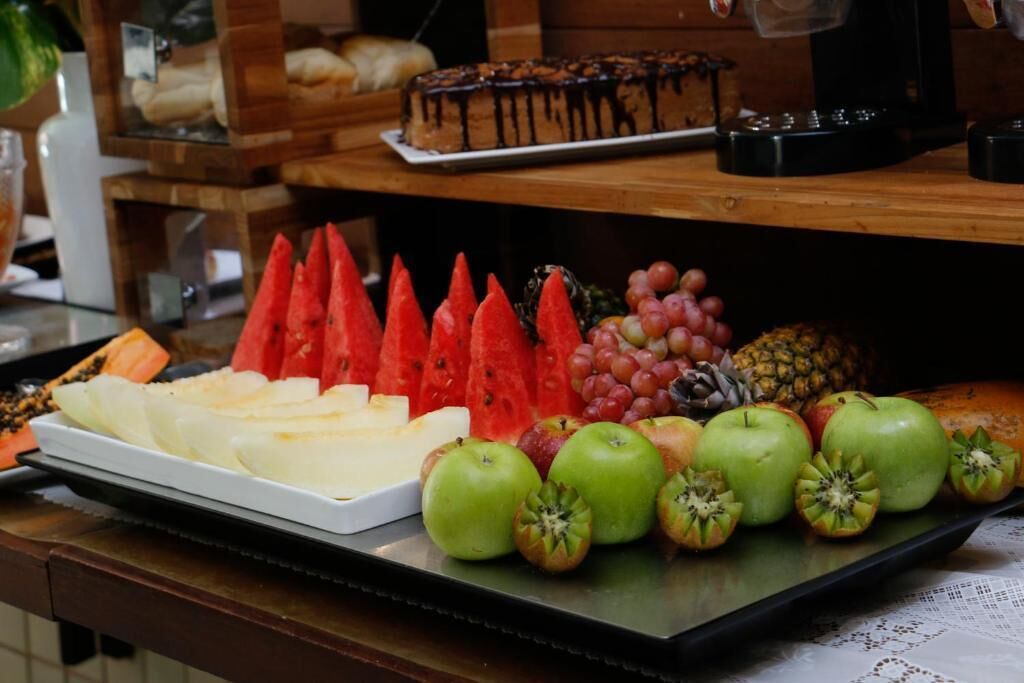 A tray of sliced cheese, watermelon, grapes, apples, and pineapple on a wooden table.