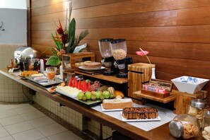 Un bufé con diversas opciones de comida, entre ellas frutas, pastelería y una estación de café.