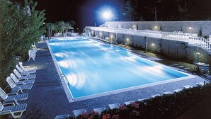 Una piscina illuminata di notte con lettini e un muro in pietra.