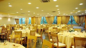 Una sala da banchetti con diversi tavoli rotondi, ognuno apparecchiato con tovaglie bianche e sedie.