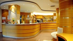 Un'area di accoglienza con un bancone in legno curvo, una macchina da caffè e un'area salotto con una panca imbottita bianca.