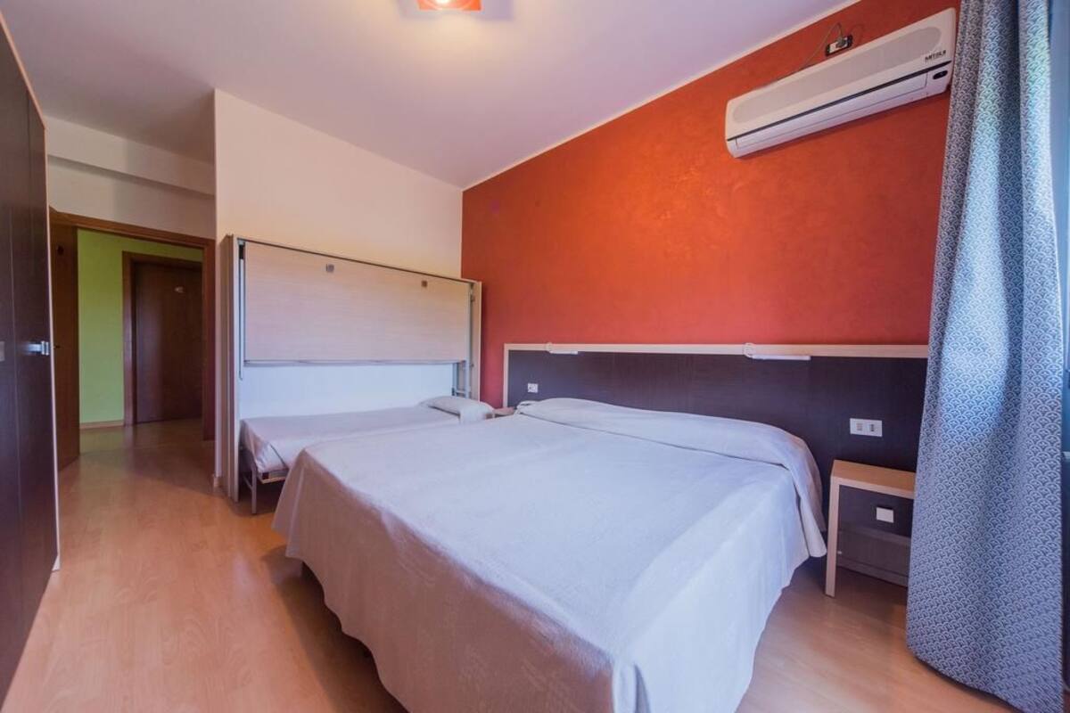 Habitación de hotel con dos camas, una pared de acento roja, un equipo de aire acondicionado y suelo de madera.