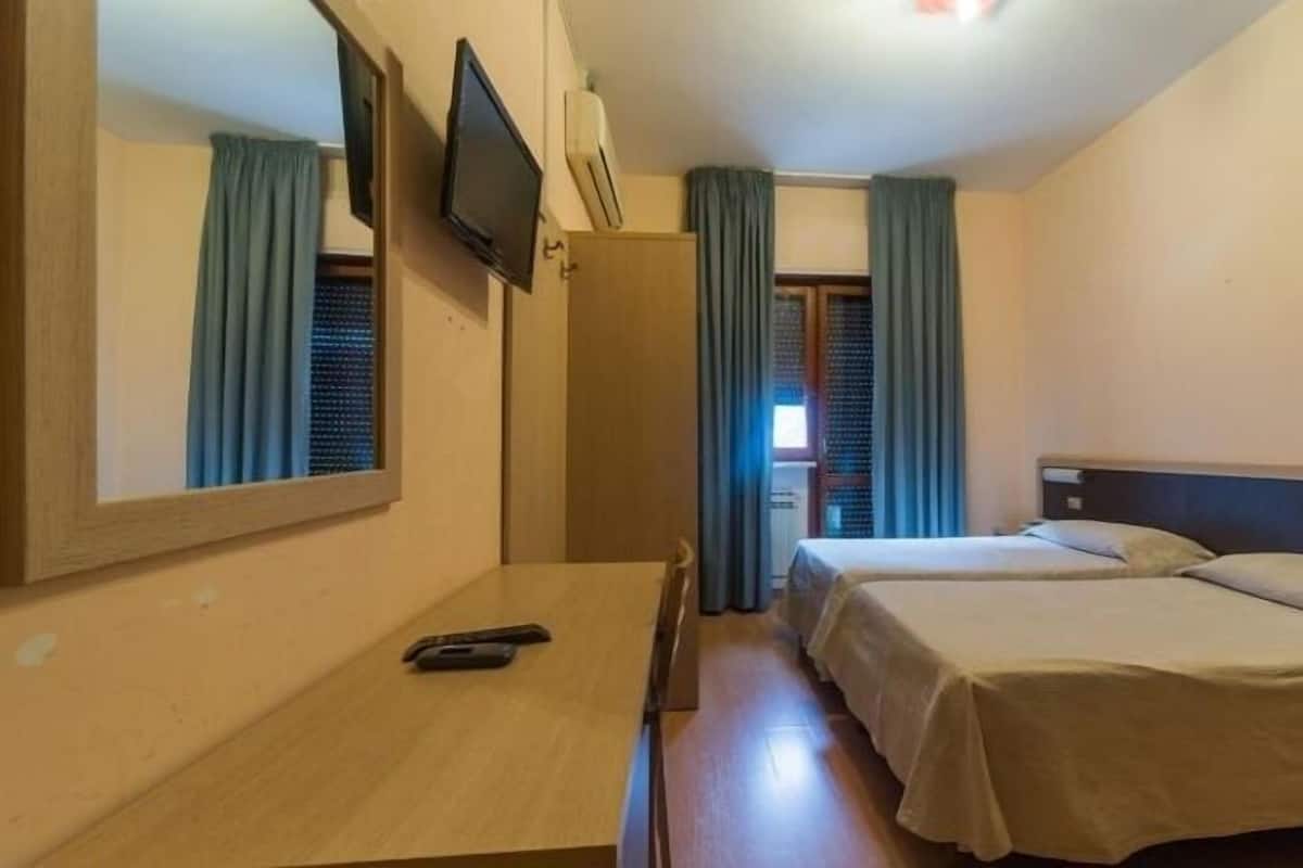 Habitación de hotel con dos camas, un escritorio, un televisor y un espejo.