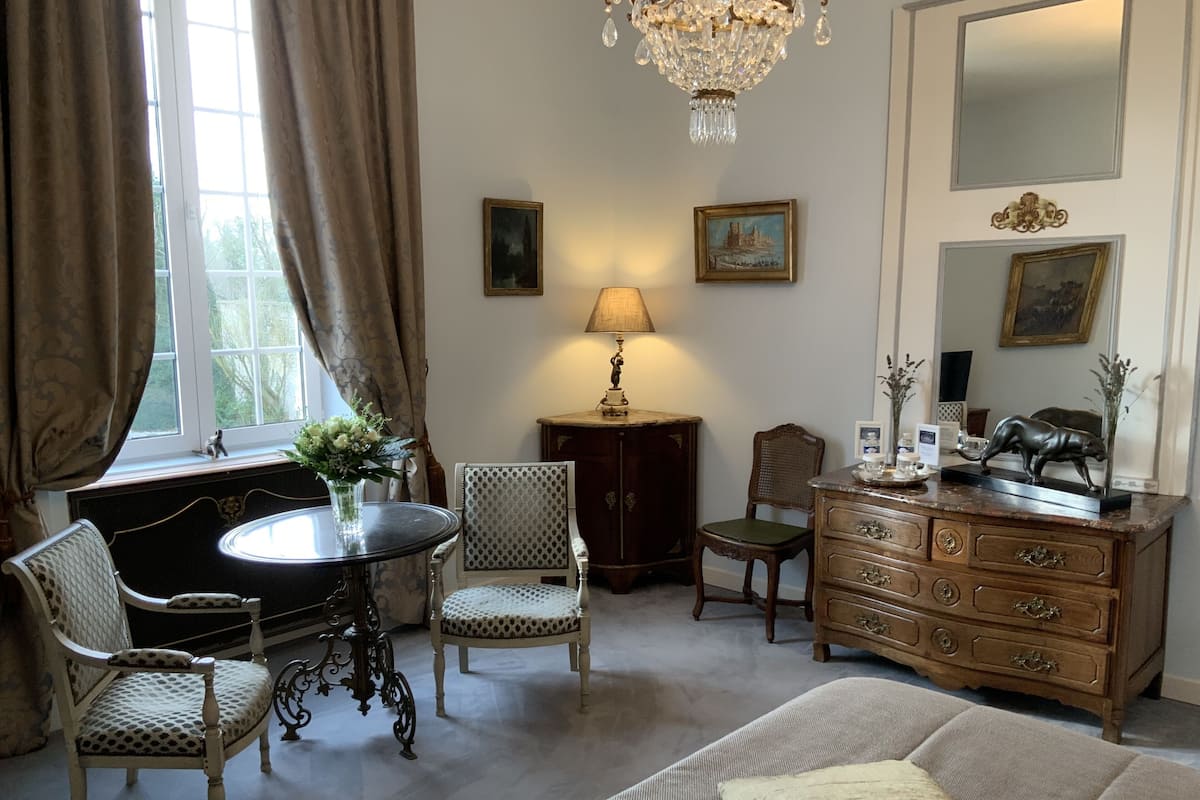 Une chambre à coucher comprenant un lit, deux chaises, une table, une commode, une lampe et un lustre.
