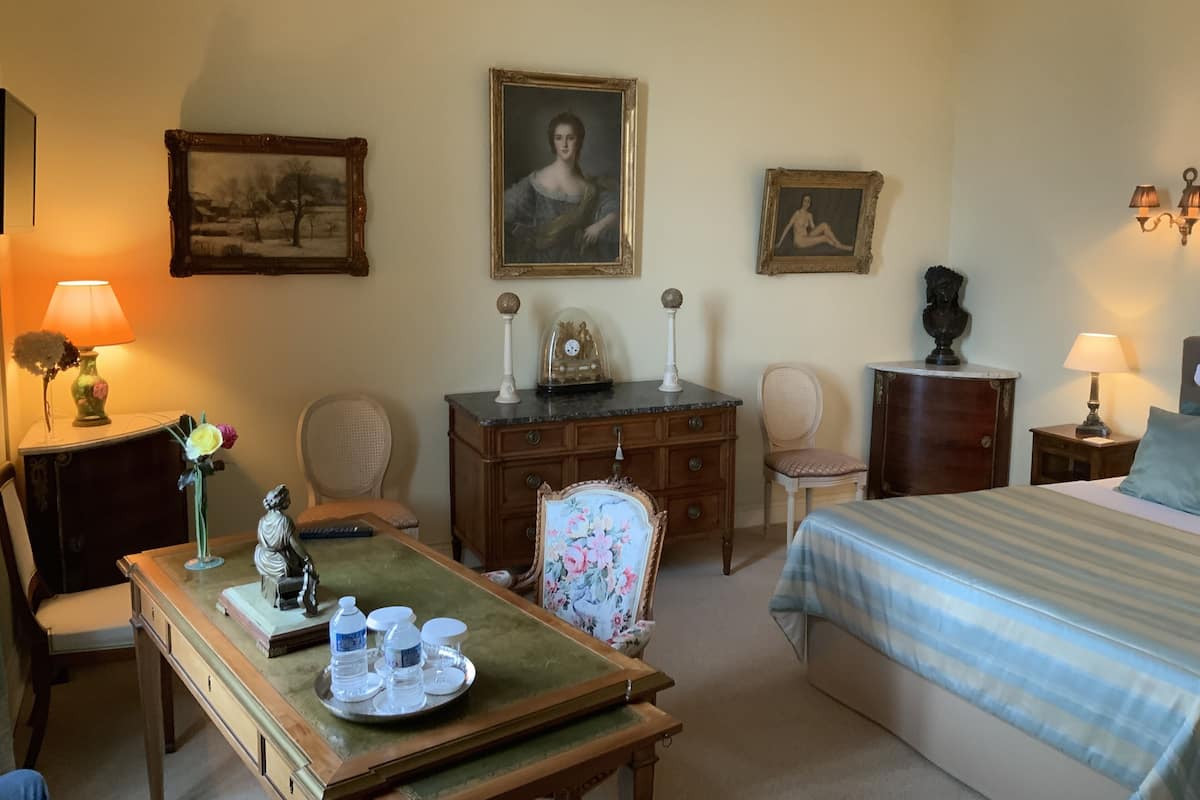 Une chambre d’hôtel avec un lit, un bureau doté d’une lampe, une chaise, une commode et deux tableaux encadrés accrochés au mur.