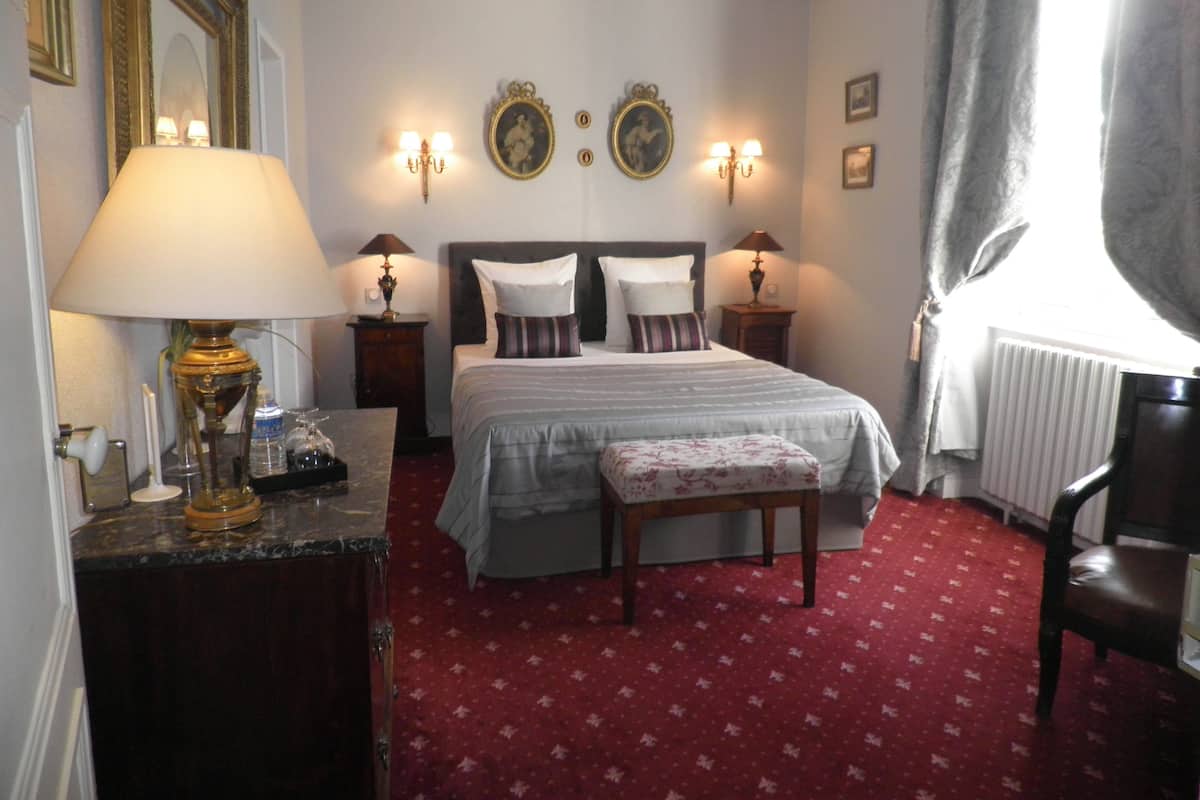 Une chambre d’hôtel avec un lit, des tables de chevet, une lampe, un miroir et une fenêtre avec des rideaux.