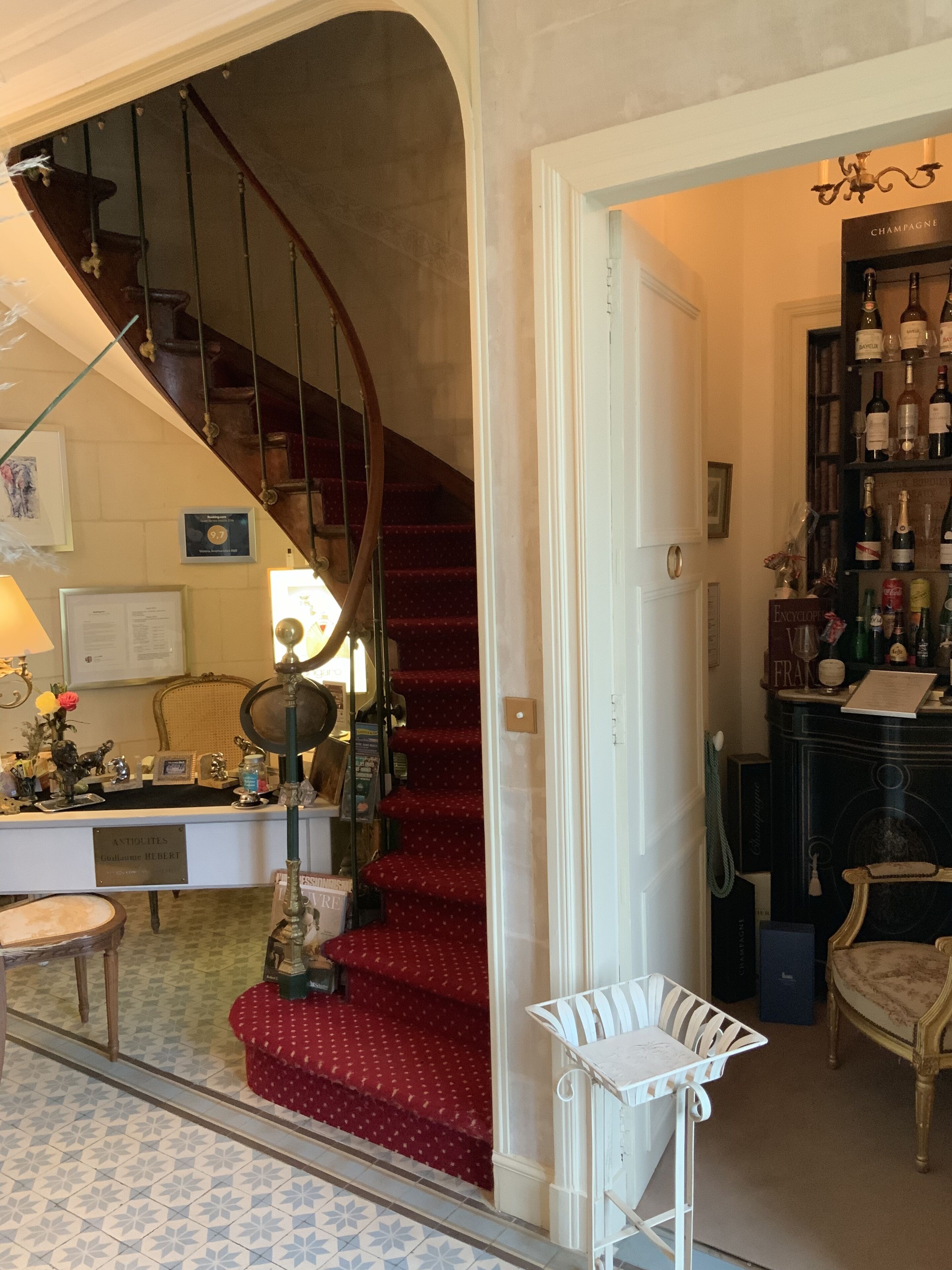 Una escalera con una alfombra roja que conduce a una habitación con un escritorio, una silla y una estantería llena de libros y botellas.