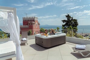 A balcony with a hot tub, a bed, and a view of the sea and a castle-like building. - Villa Garuti (Padenghe sul Garda)