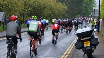 A group of cyclists on a wet road, with a motorcycle parked on the side.
