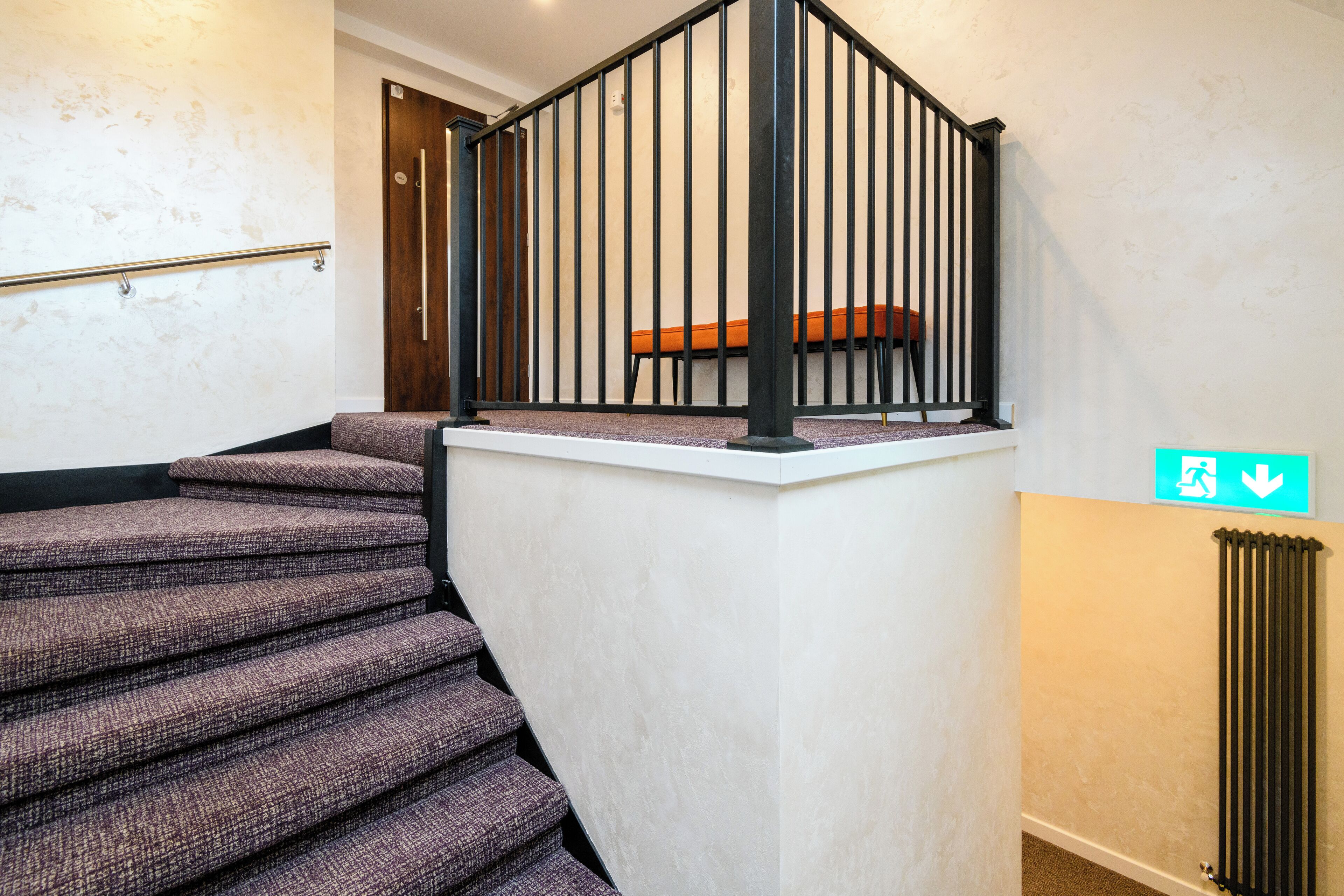 Un escalier avec une rampe noire et un banc en bois au sommet.