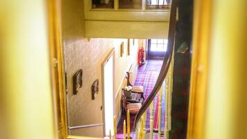 Un espejo refleja una escalera con un suelo de cuadros, un extintor y una silla.