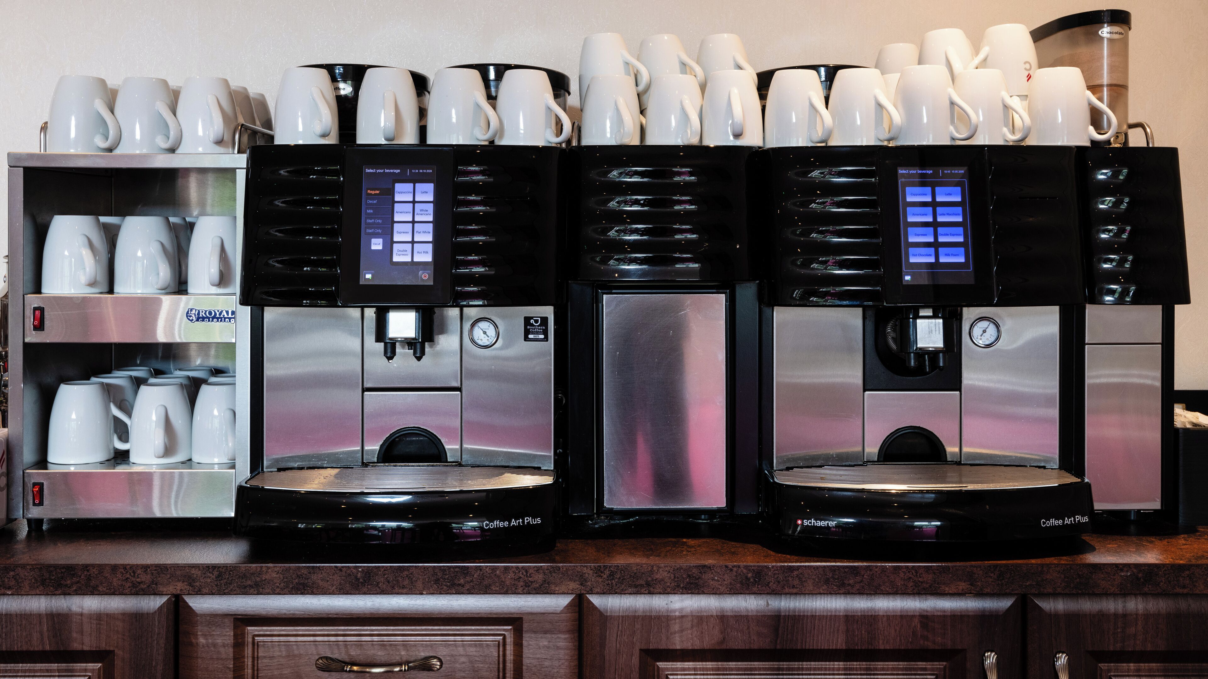 A coffee station with multiple coffee machines and a variety of coffee cups.
