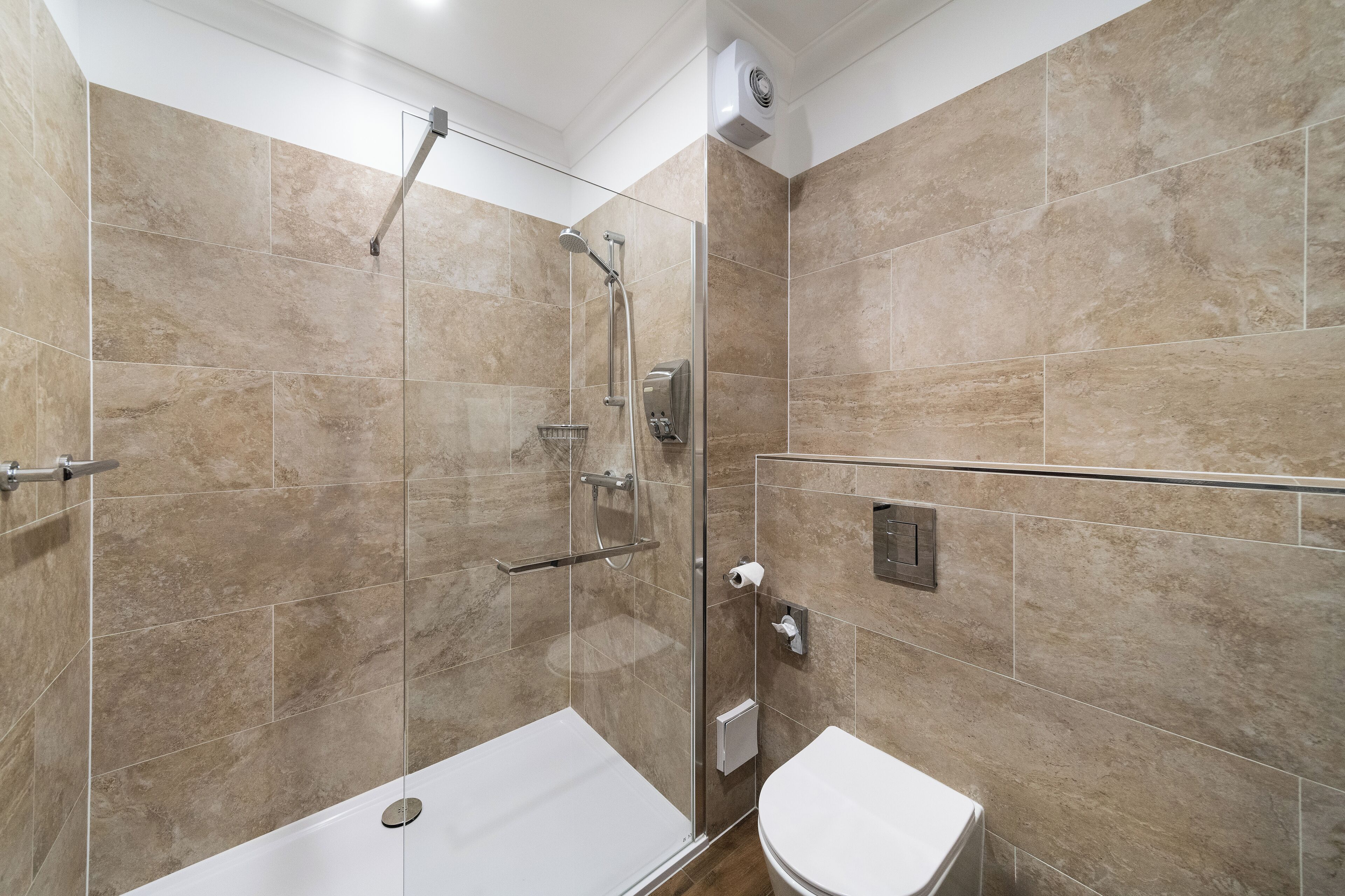 Une salle de bain moderne avec une douche à parois de verre, des toilettes blanches et des carreaux de couleur beige.