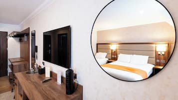 Habitación de hotel con un escritorio de madera, un espejo grande, una cama con ropa blanca y un espejo redondo que refleja la habitación.
