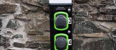 A ROLEC EV charging station with two green buttons, labeled 3 and 4, against a stone wall background.