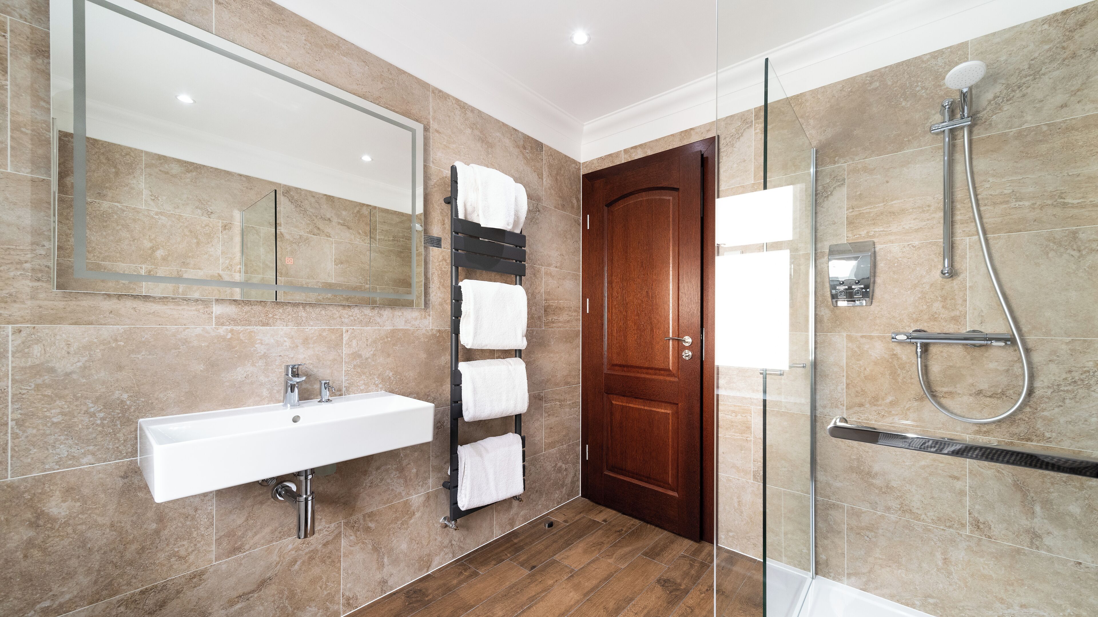 A modern bathroom with a glass shower enclosure, a built-in sink, and a wooden door.