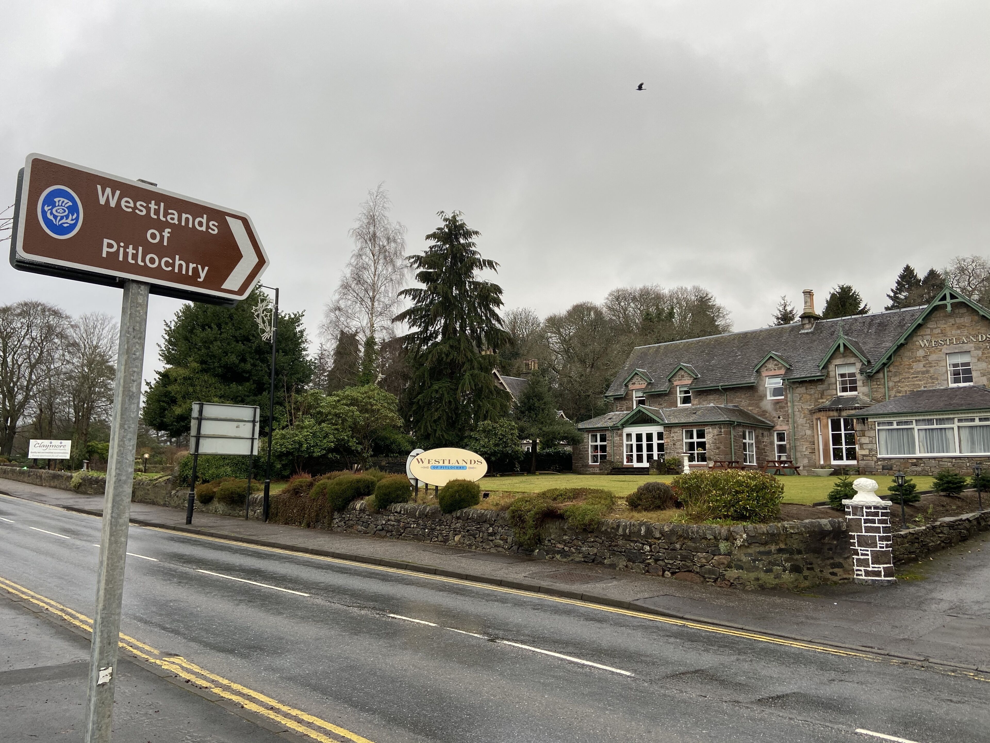 Een bord voor Westlands of Pitlochry, een stenen gebouw met een klassiek ontwerp, en een verzorgd gazon ervoor.