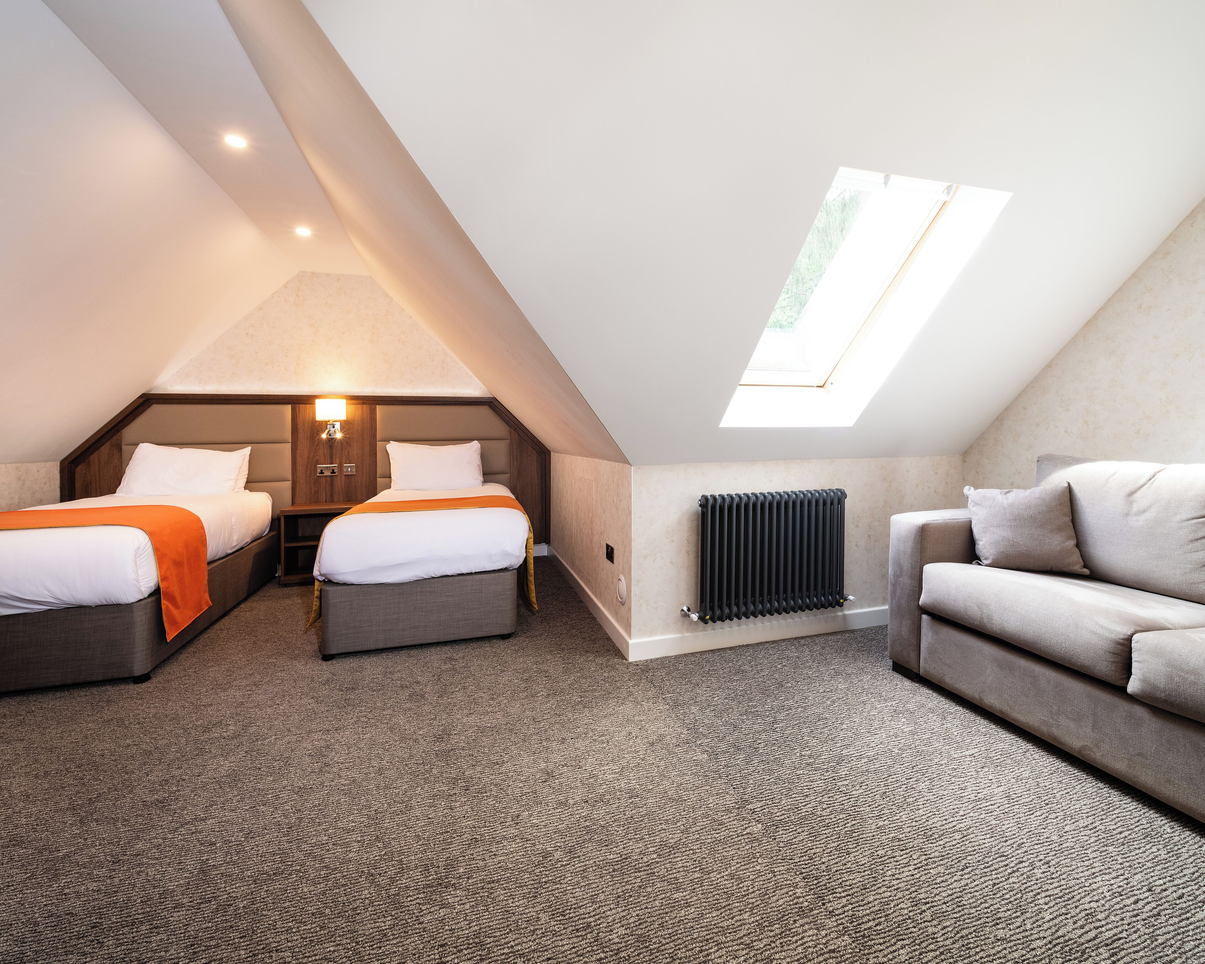 A bedroom with two beds, a sofa, a skylight, and a radiator.
