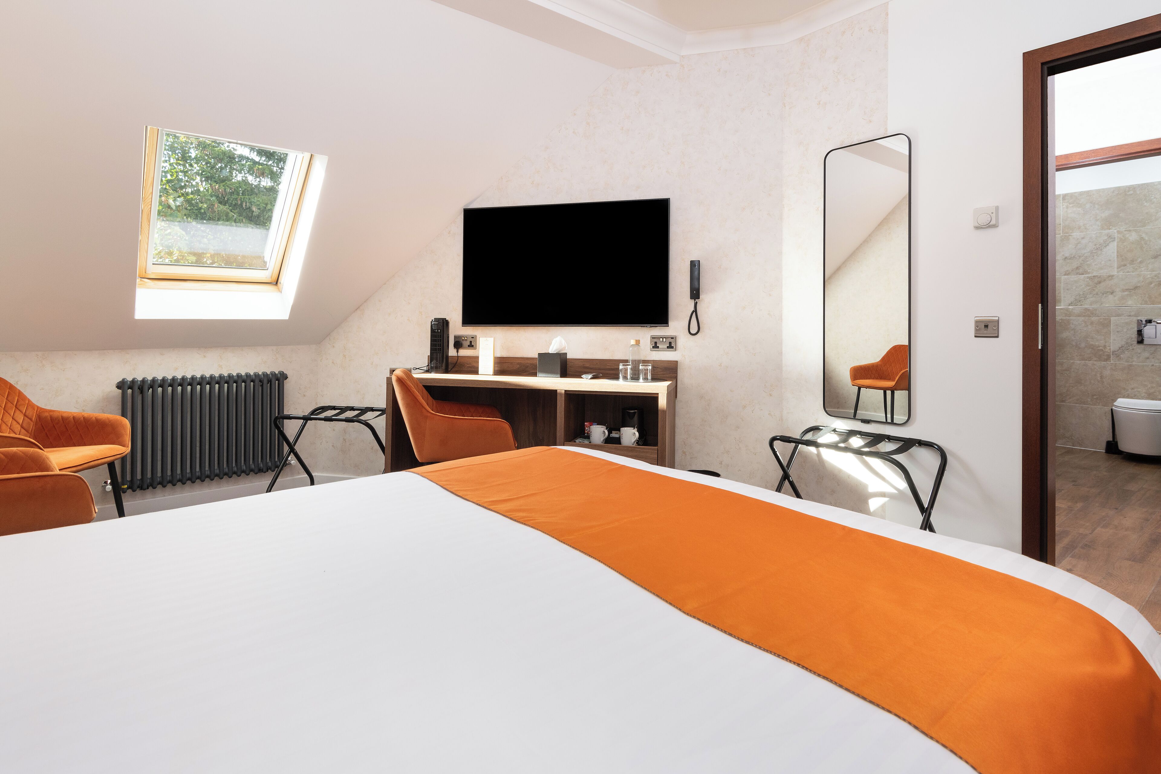 Una habitación de hotel moderna con una cama grande, un escritorio con una silla, una televisión y un tragaluz.