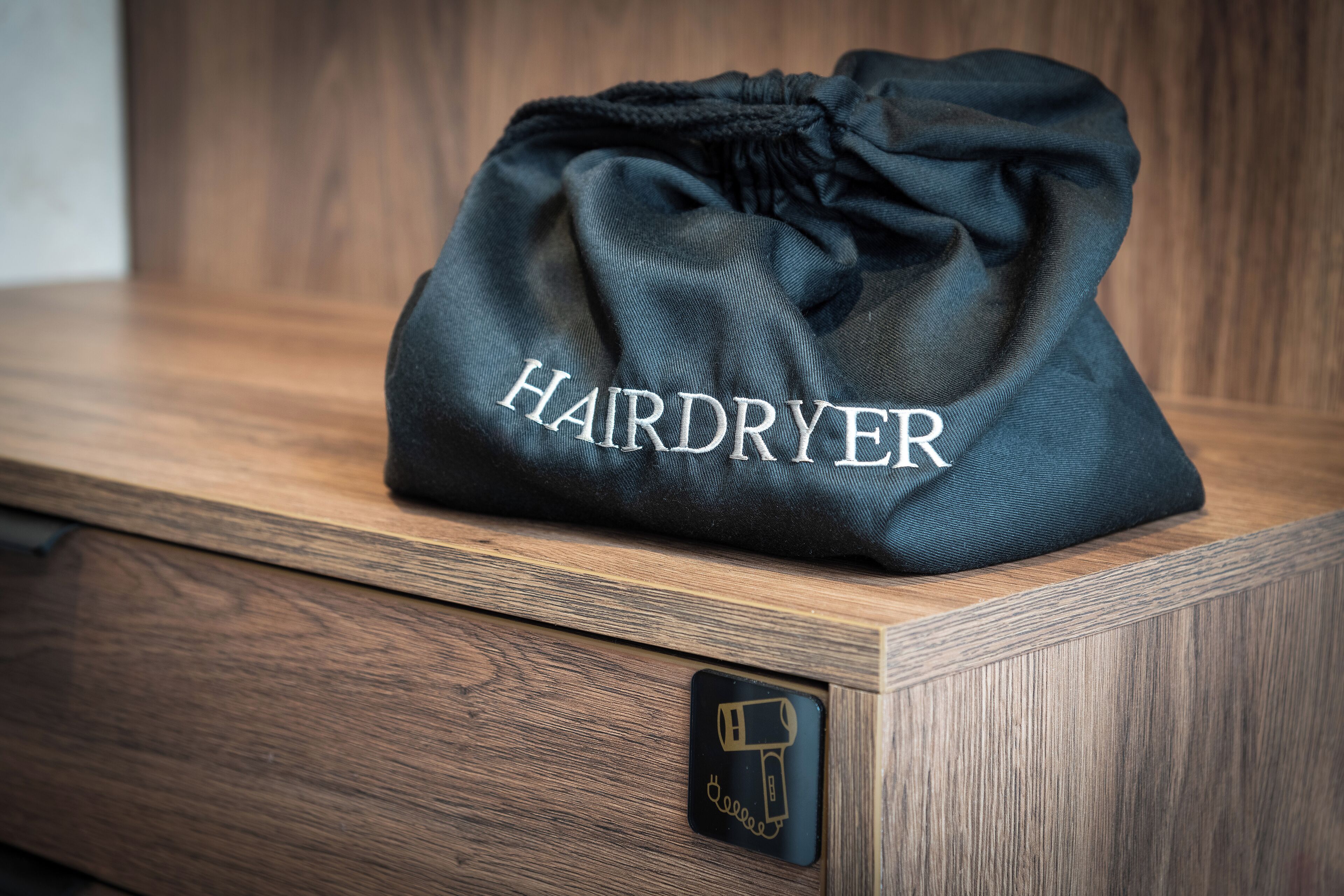 A black drawstring bag labeled "HAIRDRYER" on a wooden surface.