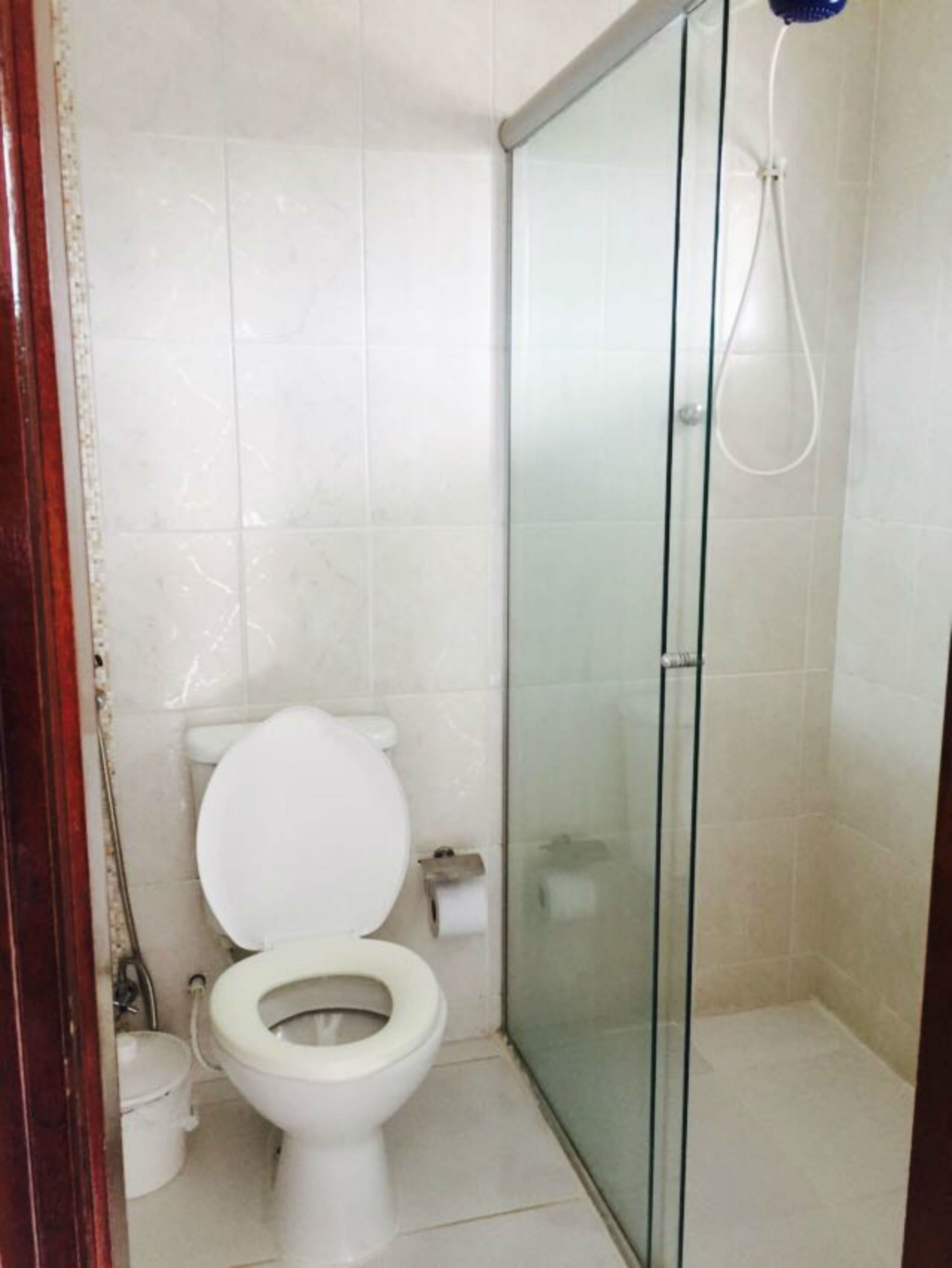 Casa de banho com sanita, cabine de duche em vidro e parede revestida a azulejos brancos.