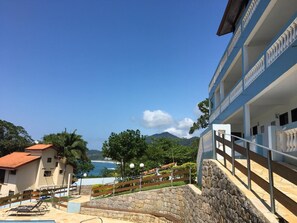 Um hotel à beira-mar com uma escadaria de pedra que dá para uma varanda, com vista para o mar e as montanhas.