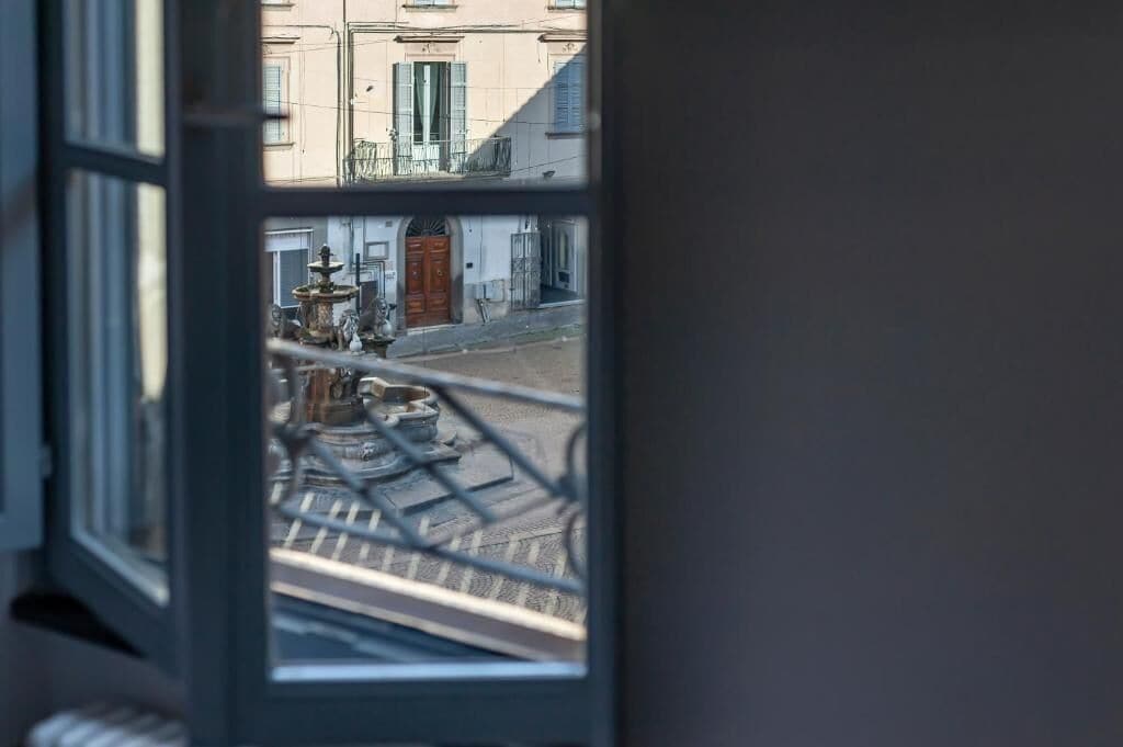 A view through a window with a metal railing, a street with buildings, and a door.