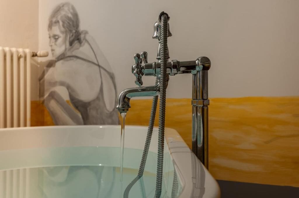 Una bañera con cabezal de ducha y manguera, un radiador, y una vista parcial de una pared donde se ve una persona.