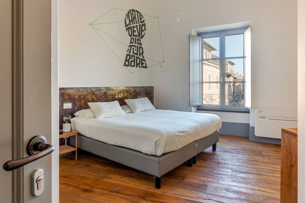 A bedroom with a bed, a window, and a geometric wall decoration.