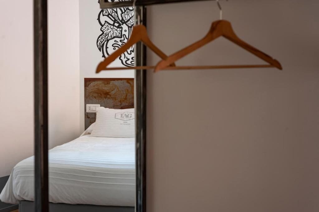 A bedroom with a bed, a wooden hanger, and a wall with a black and white abstract design.