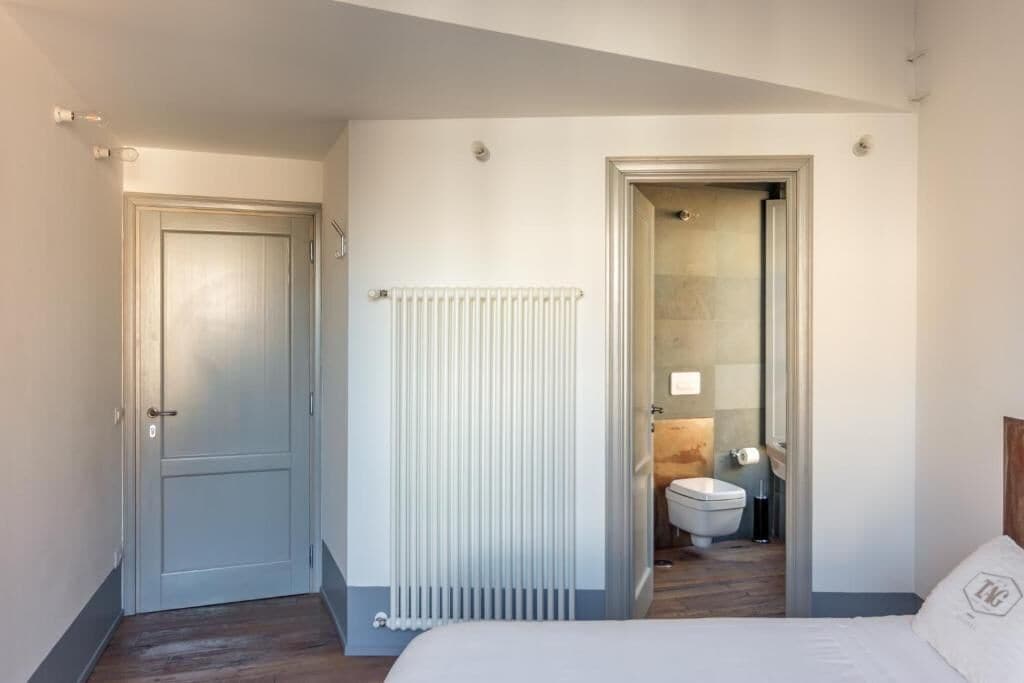 Habitación de hotel con cama, radiador, una puerta y vista al baño.