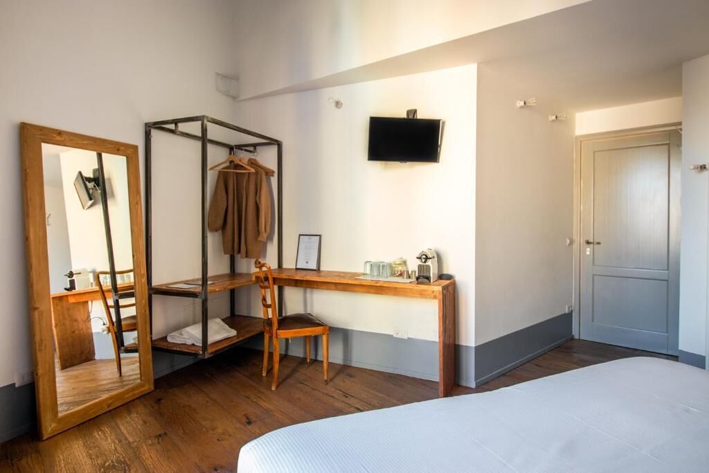 Une chambre à coucher comprenant un lit, un bureau en bois, une chaise, un porte-manteau suspendu, un miroir et un téléviseur.
