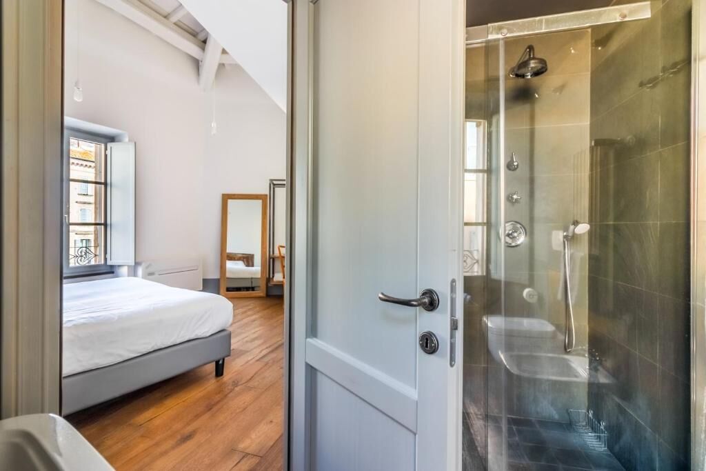 Un dormitorio con cama, piso de madera y una puerta que da a un área de ducha con cabina de vidrio.