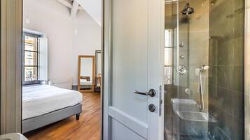 Un dormitorio con cama, piso de madera y una puerta que da a un área de ducha con cabina de vidrio.