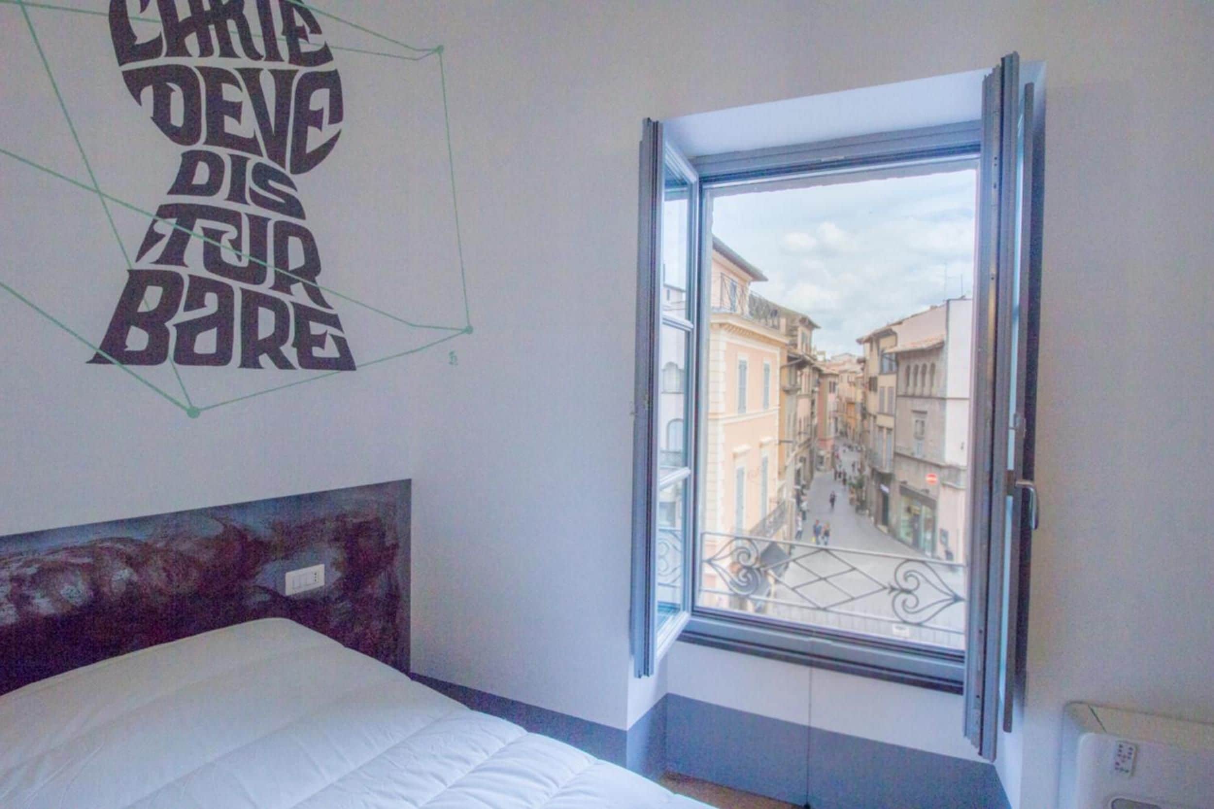 A bedroom with a bed, a window with a view of a street, and a wall with a geometric design.