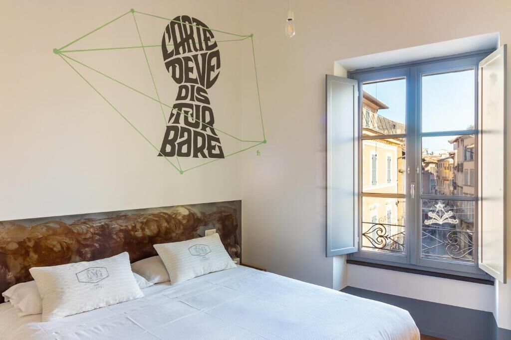 Ein Schlafzimmer mit einem Bett, einem Wandbild und einem Fenster mit Blick auf Gebäude.