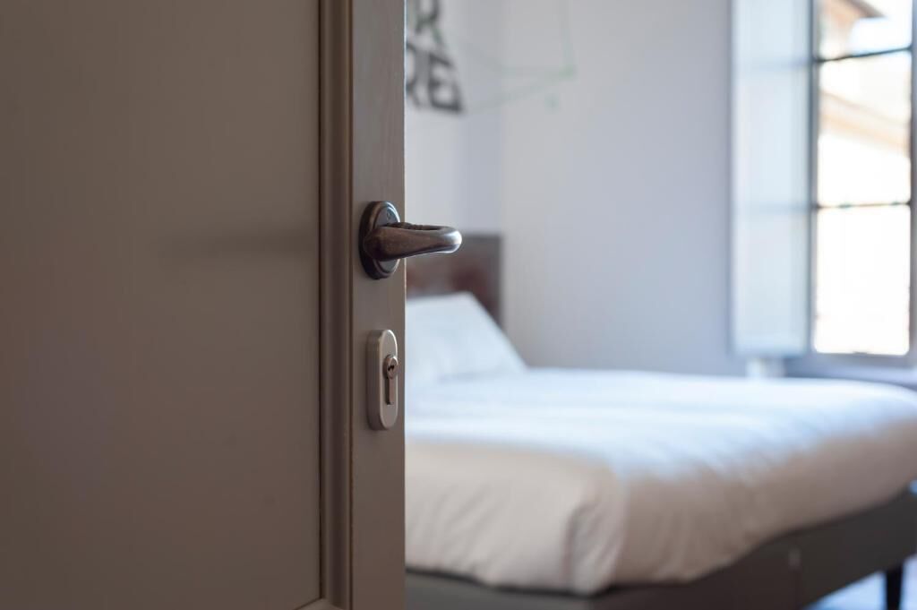 Puerta con cerradura y manija, que da acceso a una cama con ropa blanca.