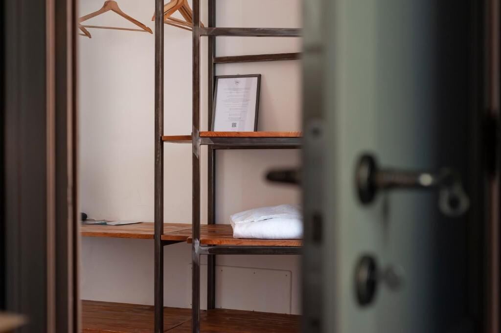 Ein Zimmer mit Holzboden, einem Metallregal, einem hängenden Kleidungsstück und einem gerahmten Zertifikat auf dem Regal.