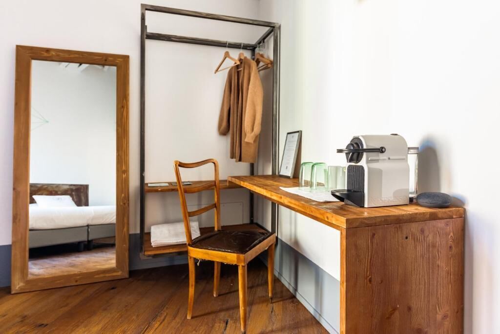 Una habitación compacta con un escritorio de madera, una silla, una cama con cabecera de madera, un perchero y un espejo.