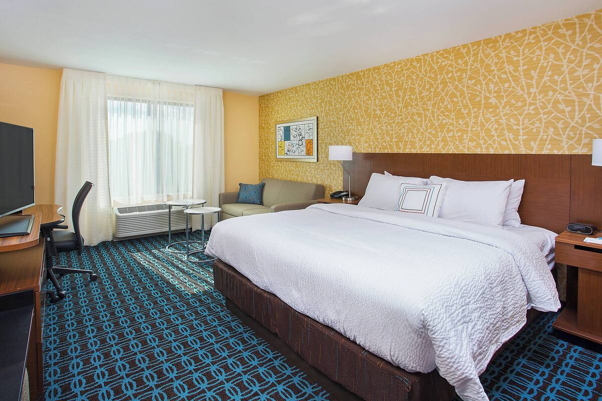 A hotel room with a large bed, a desk with a computer, a chair, and a small table.
