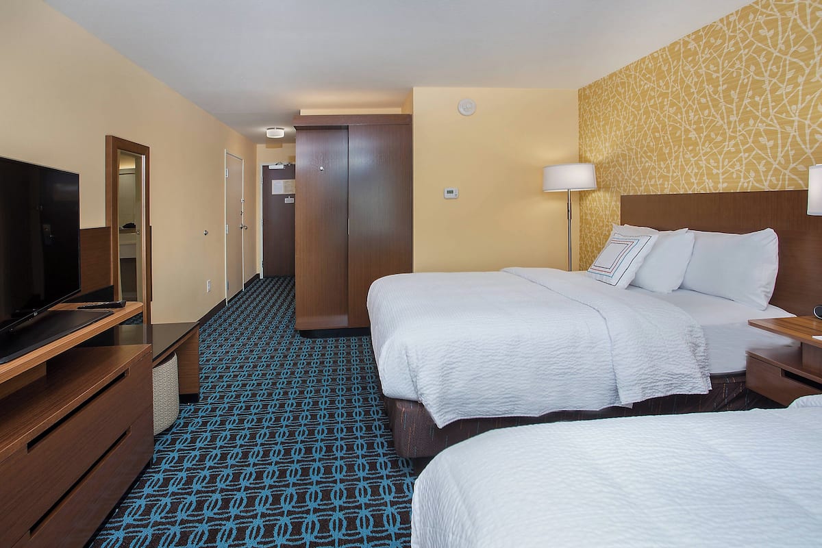A hotel room with two beds, a TV, a desk, and a patterned carpet.