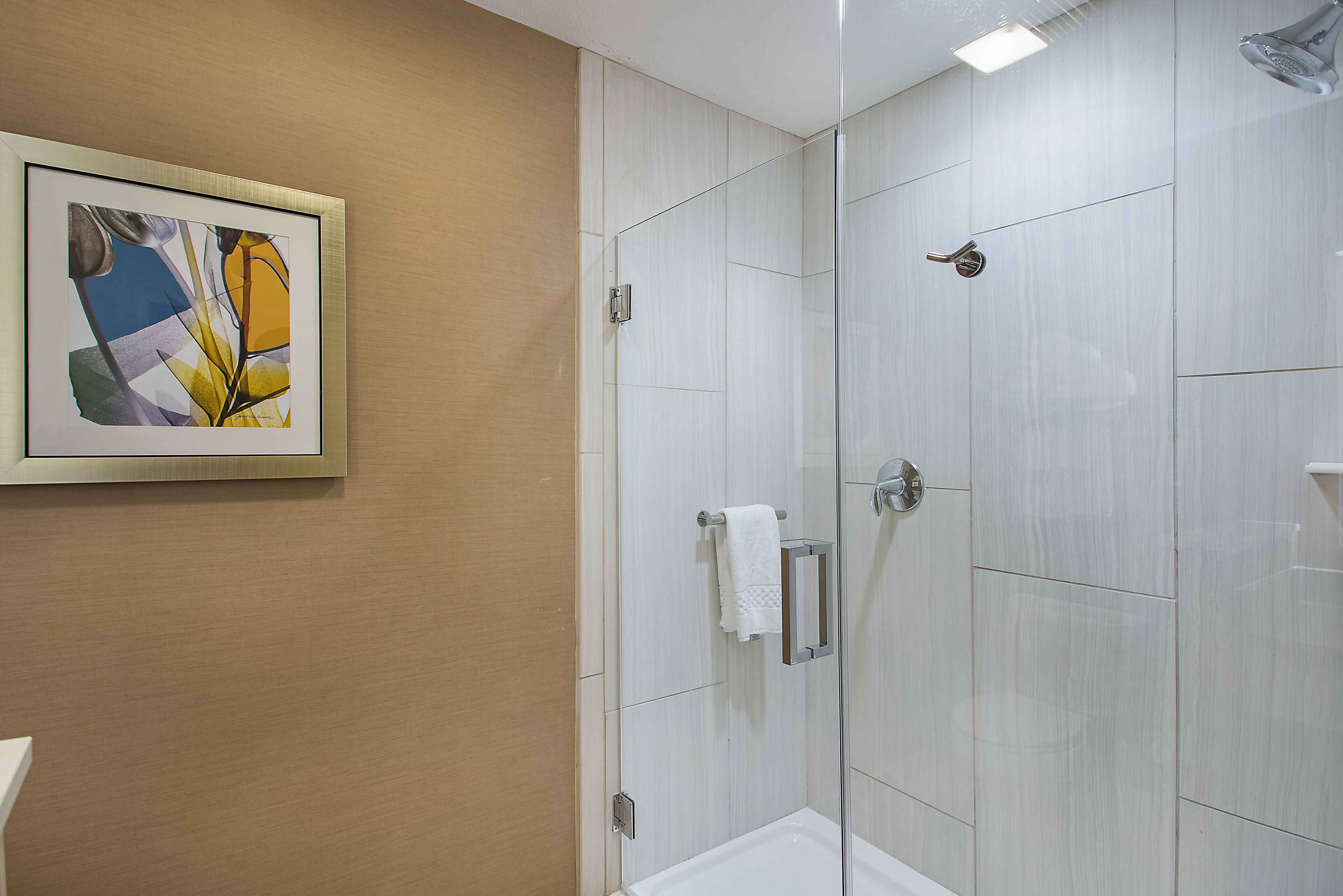 A modern bathroom with a glass shower enclosure, a framed abstract artwork on the wall, and a towel rack.