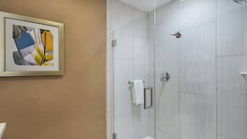 A modern bathroom with a glass shower enclosure, a framed abstract artwork on the wall, and a towel rack.